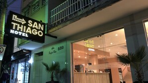 De gevel van Hotel San Thioiago, met een duidelijke ingang, een grote potplant en een bord met de naam en het adres van het hotel.