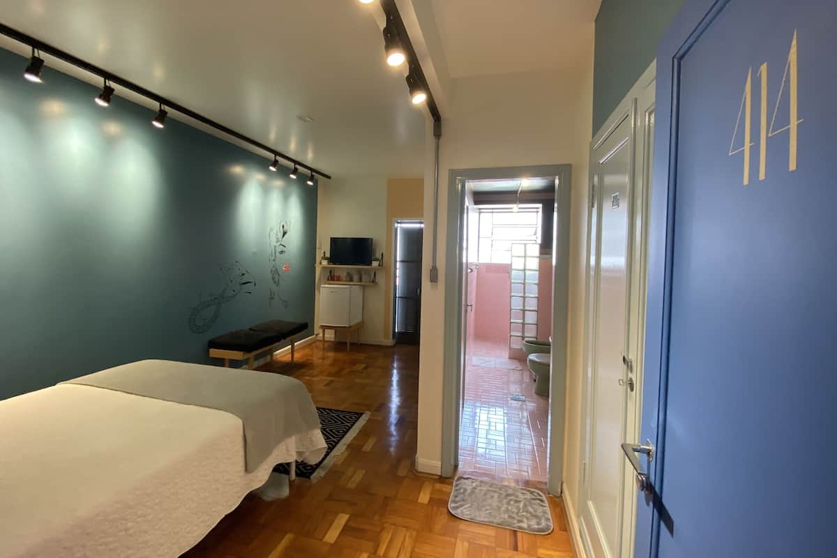 A room with a bed, a bench, a small TV, and a door leading to another room.