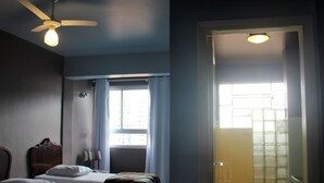 Een slaapkamer met een bed, een plafondventilator en een raam met gordijnen.