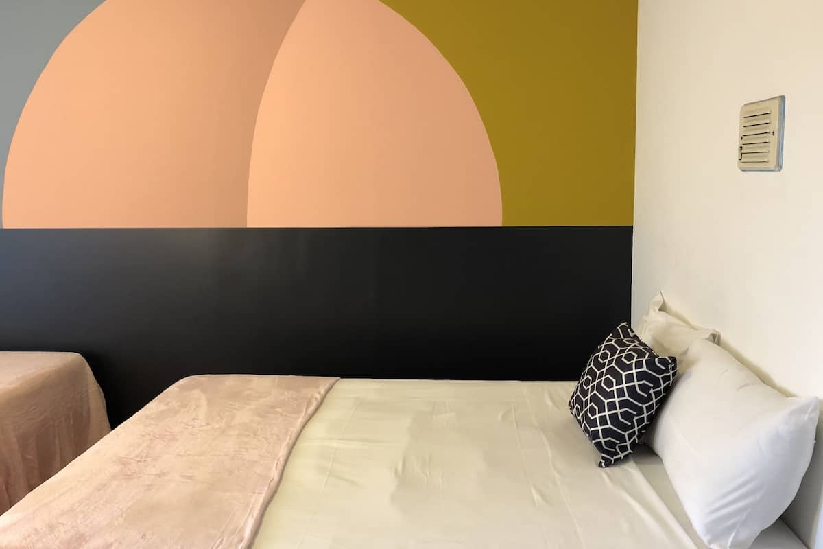 A bedroom with a bed, pillows, a headboard, and a wall with a geometric design.