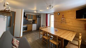 Une cuisine chaleureuse avec des meubles en bois, un four à micro-ondes et un réfrigérateur. On y trouve une table à manger avec des chaises, ainsi qu'un mur en bois orné d'une horloge et de quelques décorations.