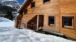 Un chalet en bois doté de nombreuses fenêtres et d’une entrée abritée, entouré de neige.