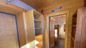 Un intérieur en bois avec un lit superposé, des étagères ouvertes et une enseigne indiquant « COL DES MARCHÉS ».