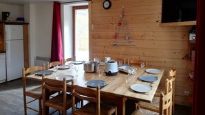 Une table de salle à manger en bois, mise avec des assiettes, des verres et une bouilloire.