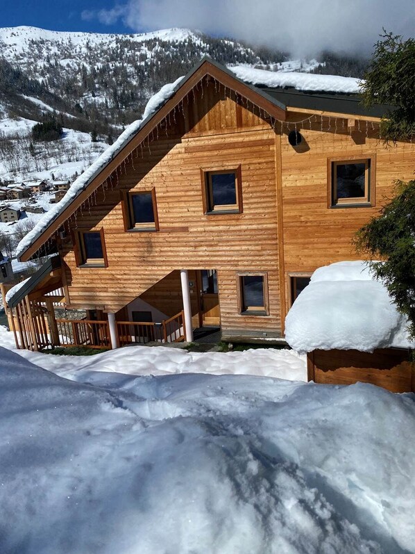 A wooden chalet with a sloped roof, multiple windows, and a snow-covered landscape in the background. - Gîtes 2+3 - 20 guests - 8 cozy rooms - sauna - panoramic balconies (VALMEINIER)