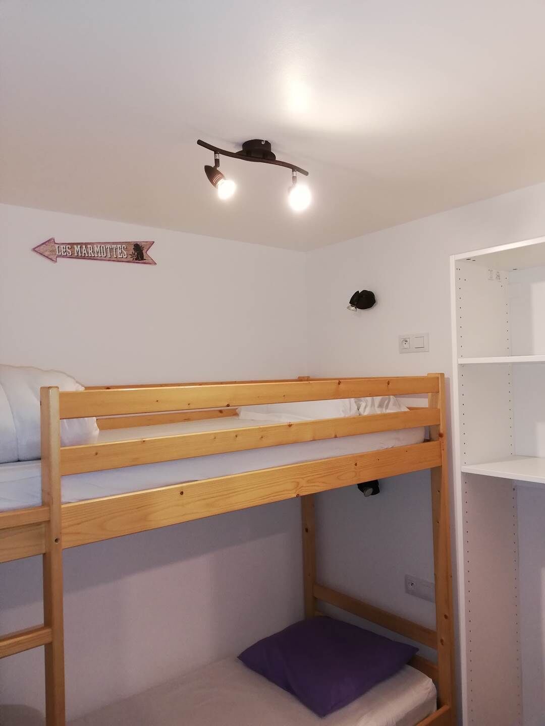 Une chambre avec des lits superposés, un panneau accroché au mur et une étagère.