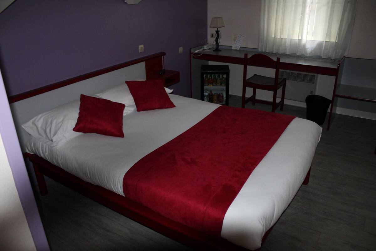 A hotel room with a bed, a desk, a chair, and a small refrigerator.