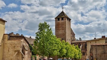 A historic town square with a prominent tower, cobblestone streets, and parked vehicles.