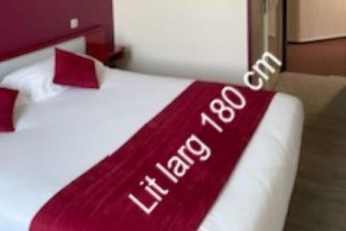 A hotel room with a large bed, a red throw blanket, and a small bedside table.