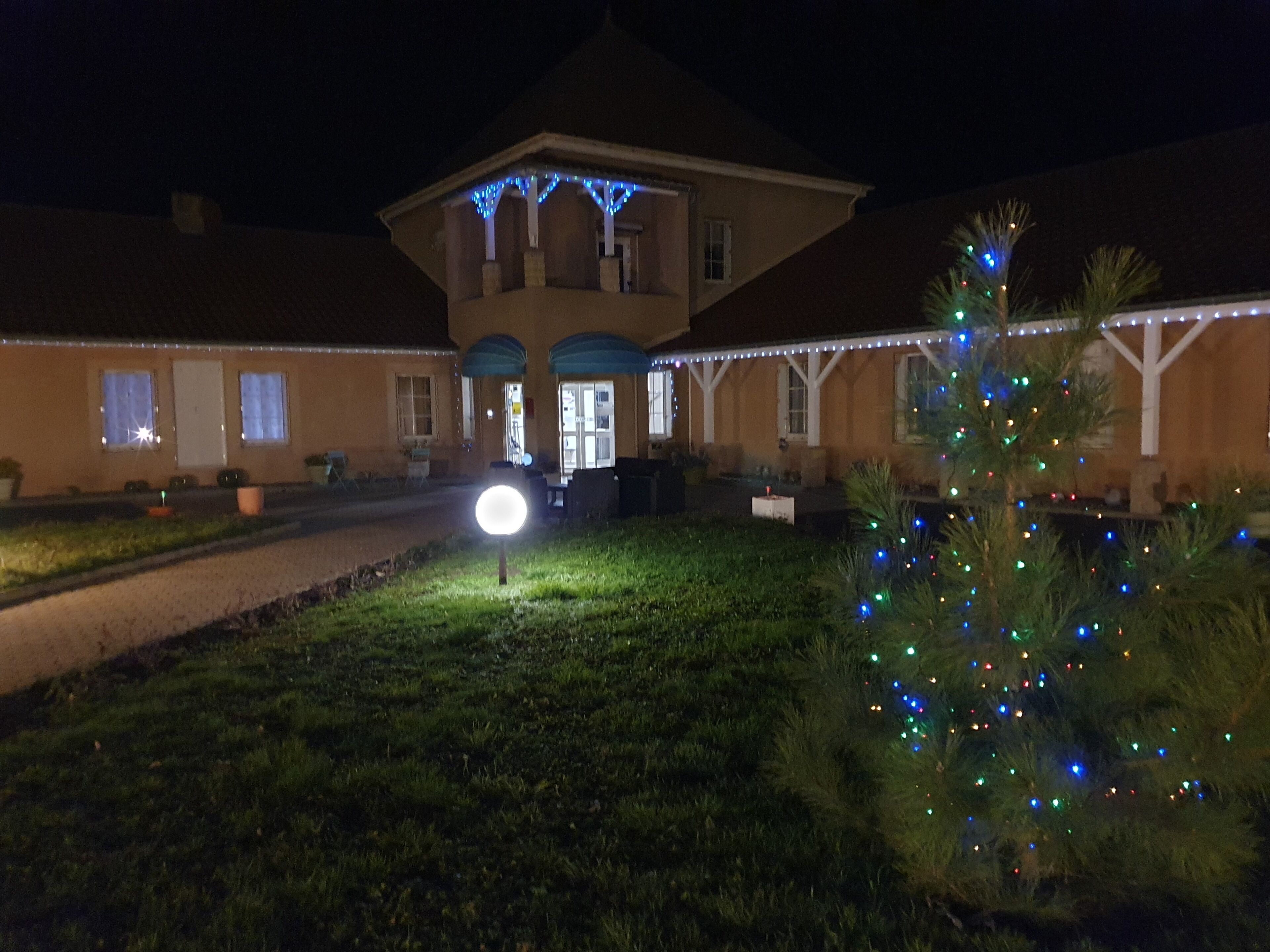 A building with a covered patio area, a well-lit entrance, and a Christmas tree decorated with lights.