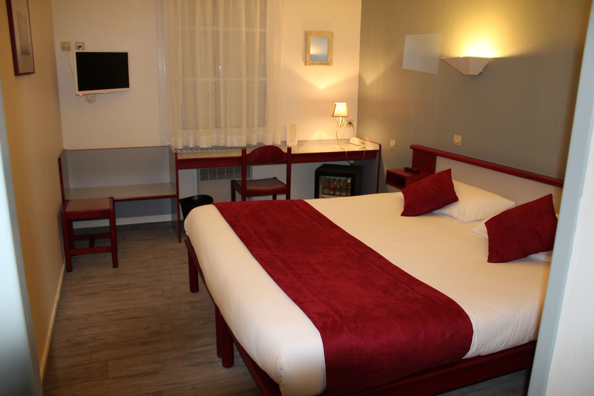 Een hotelkamer met een bed, een bureau, een stoel, een televisie en een raam met gordijnen.