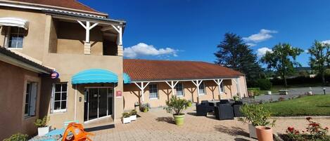 A building with a covered patio area, outdoor seating, and potted plants.