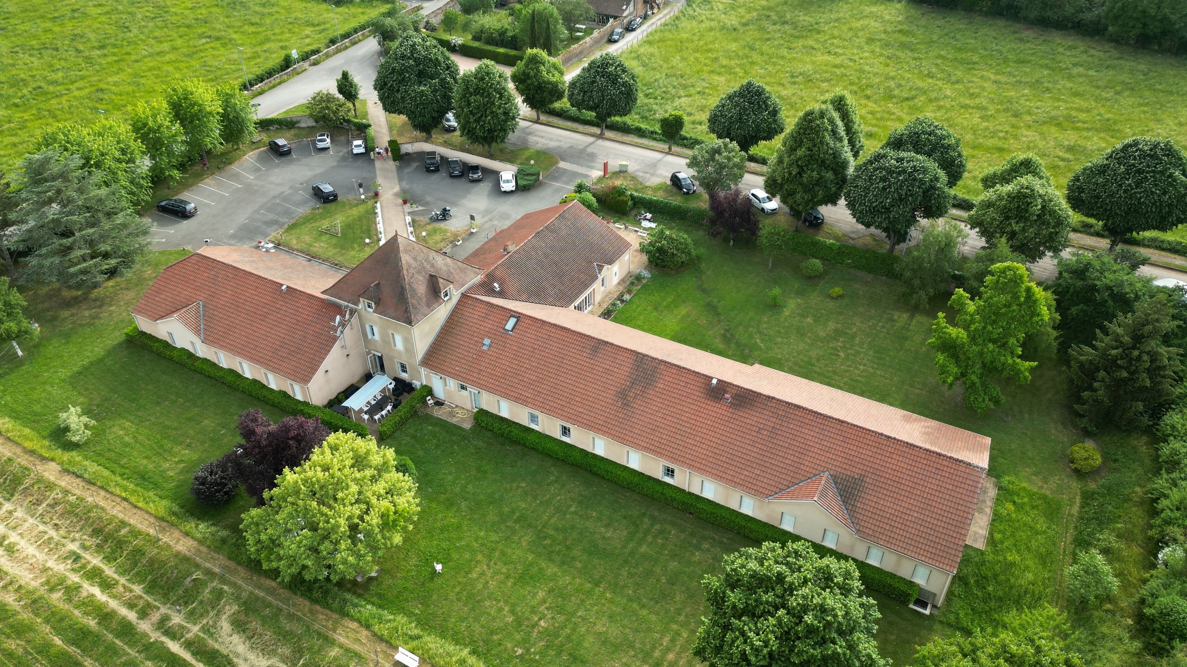 An aerial view of a large, rectangular building with a red-tiled roof, surrounded by green lawns and trees.