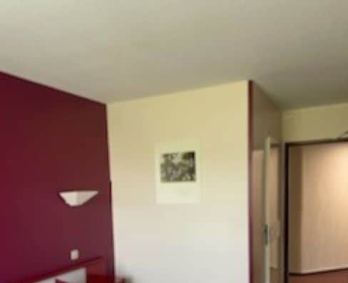 A hotel room with a large bed, a red throw blanket, and a small bedside table.
