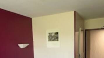 A hotel room with a large bed, a red throw blanket, and a small bedside table.