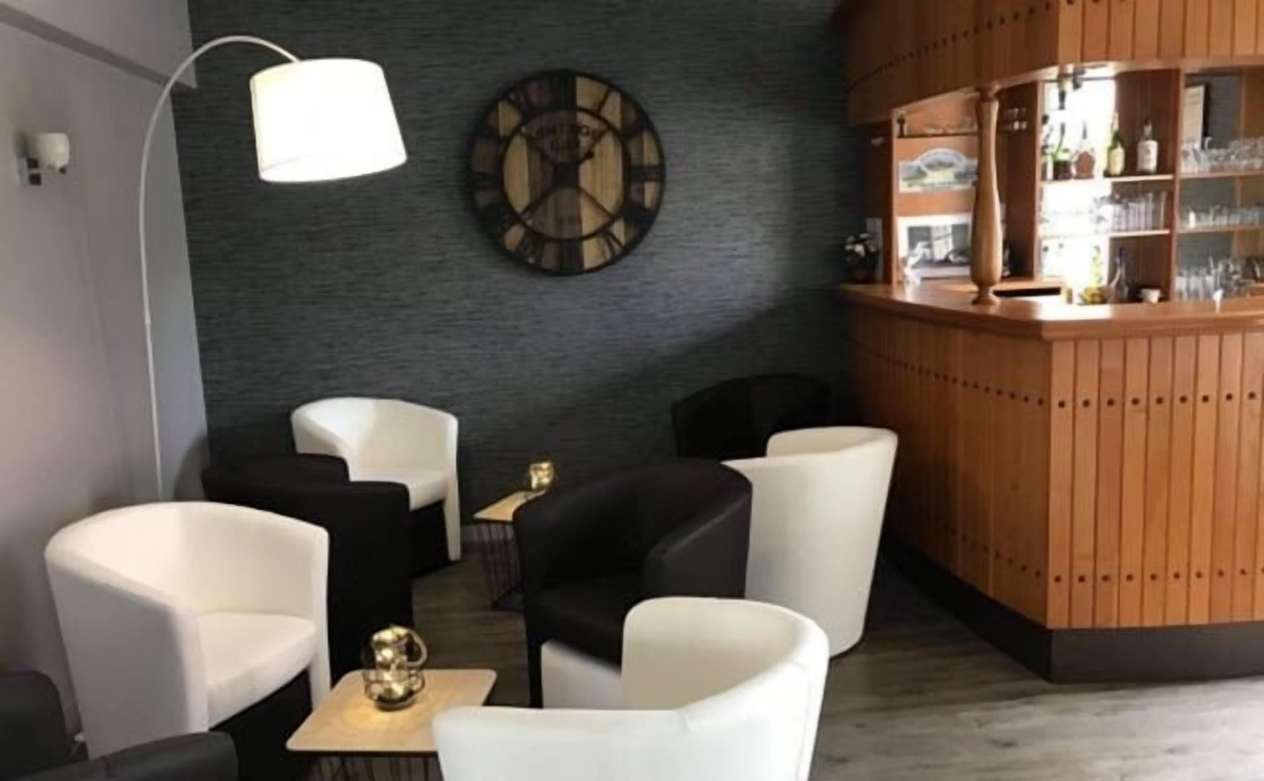 Un espace lounge moderne avec des chaises noires et blanches, un bar en bois et une grande horloge murale.