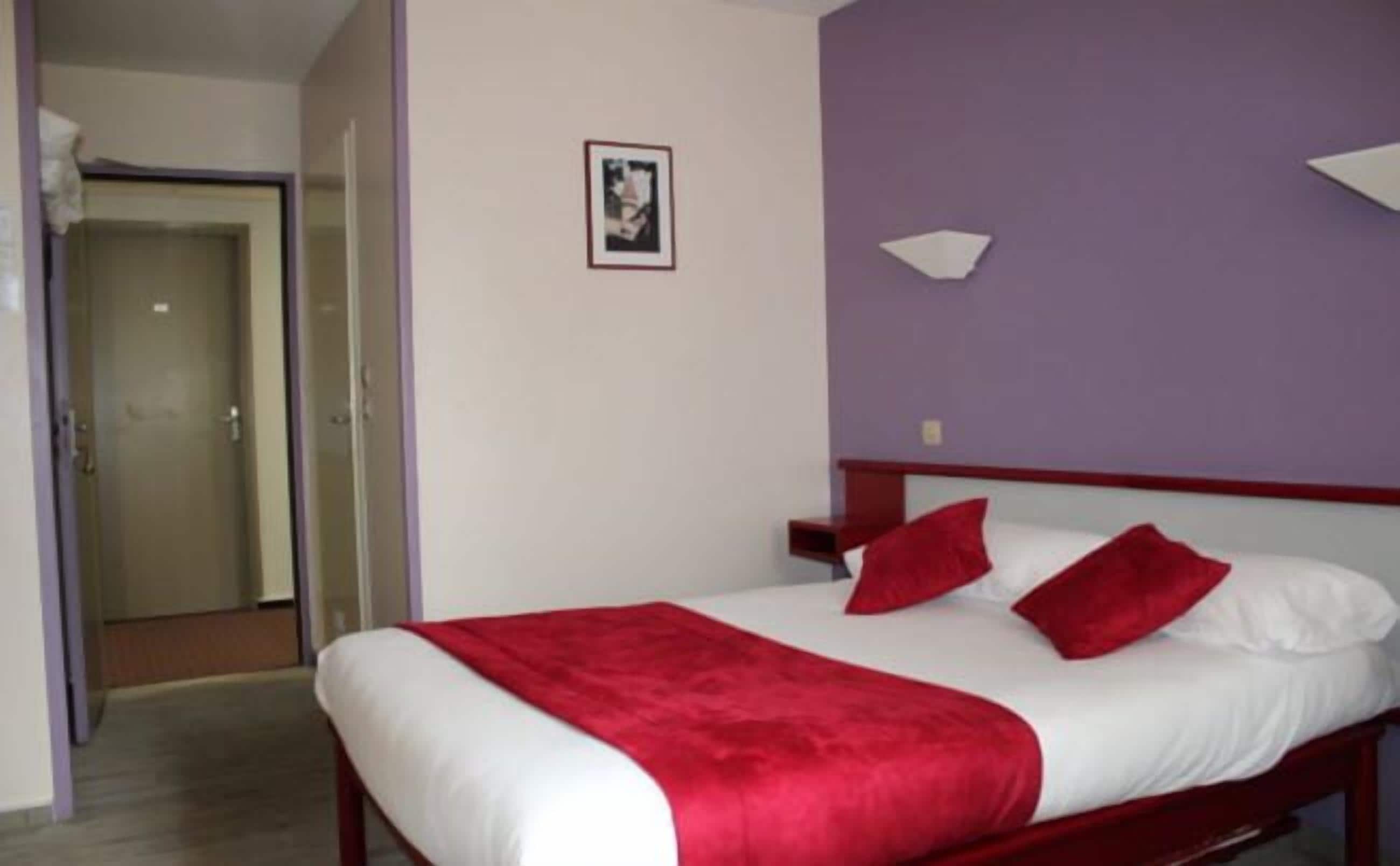 A hotel room with a bed, a red throw blanket, and a white pillow.