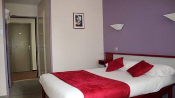 A hotel room with a bed, a red throw blanket, and a white pillow.