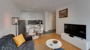 A modern living room with a sofa, a dining area, a kitchen, and a TV on a white stand. - 🎖 Le Chevène - 2 or 4 person apartment with balcony in Annecy Centre (Annecy)