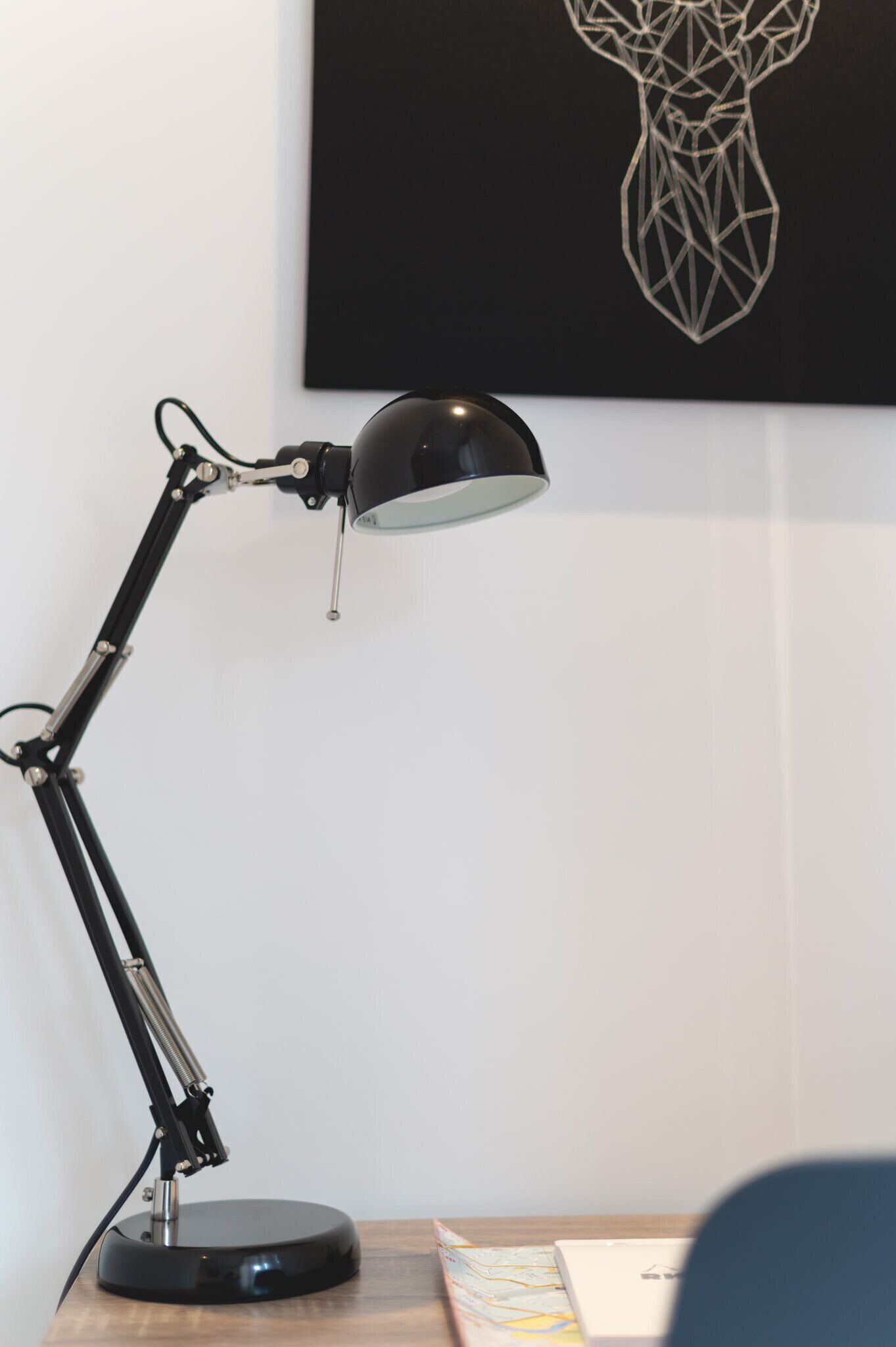 A desk lamp with a flexible arm and a round base, positioned on a wooden surface.