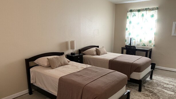 A room with two beds, a desk, and a window with curtains. - Sebastian Gardens Inn & Suites (Sebastian)