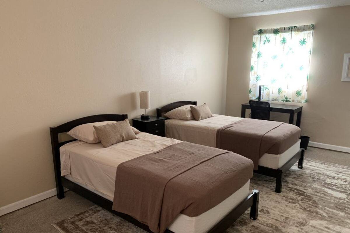 A room with two beds, a desk, and a window with curtains.