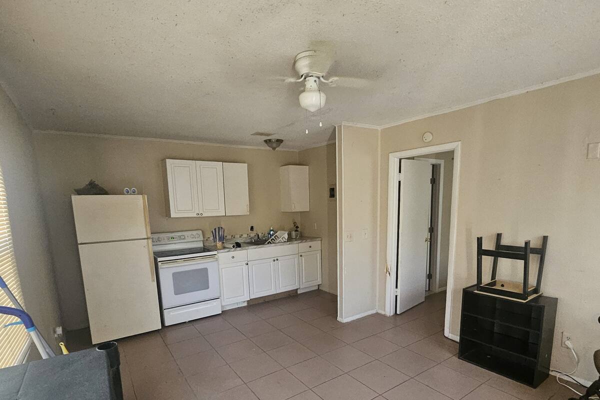A kitchen with white cabinets, a stove, and a ceiling fan.