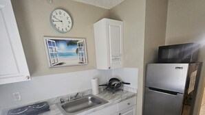 A kitchen with white cabinets, a stainless steel refrigerator, a microwave, a sink, and a clock on the wall. - Sebastian Gardens Inn & Suites (Sebastian)