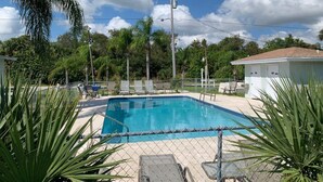 A swimming pool with a chain-link fence, surrounded by palm trees and lounge chairs. - Sebastian Gardens Inn & Suites (Sebastian)