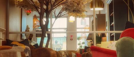 A cozy lounge area with a large artificial tree, comfortable seating, and modern pendant lighting.
