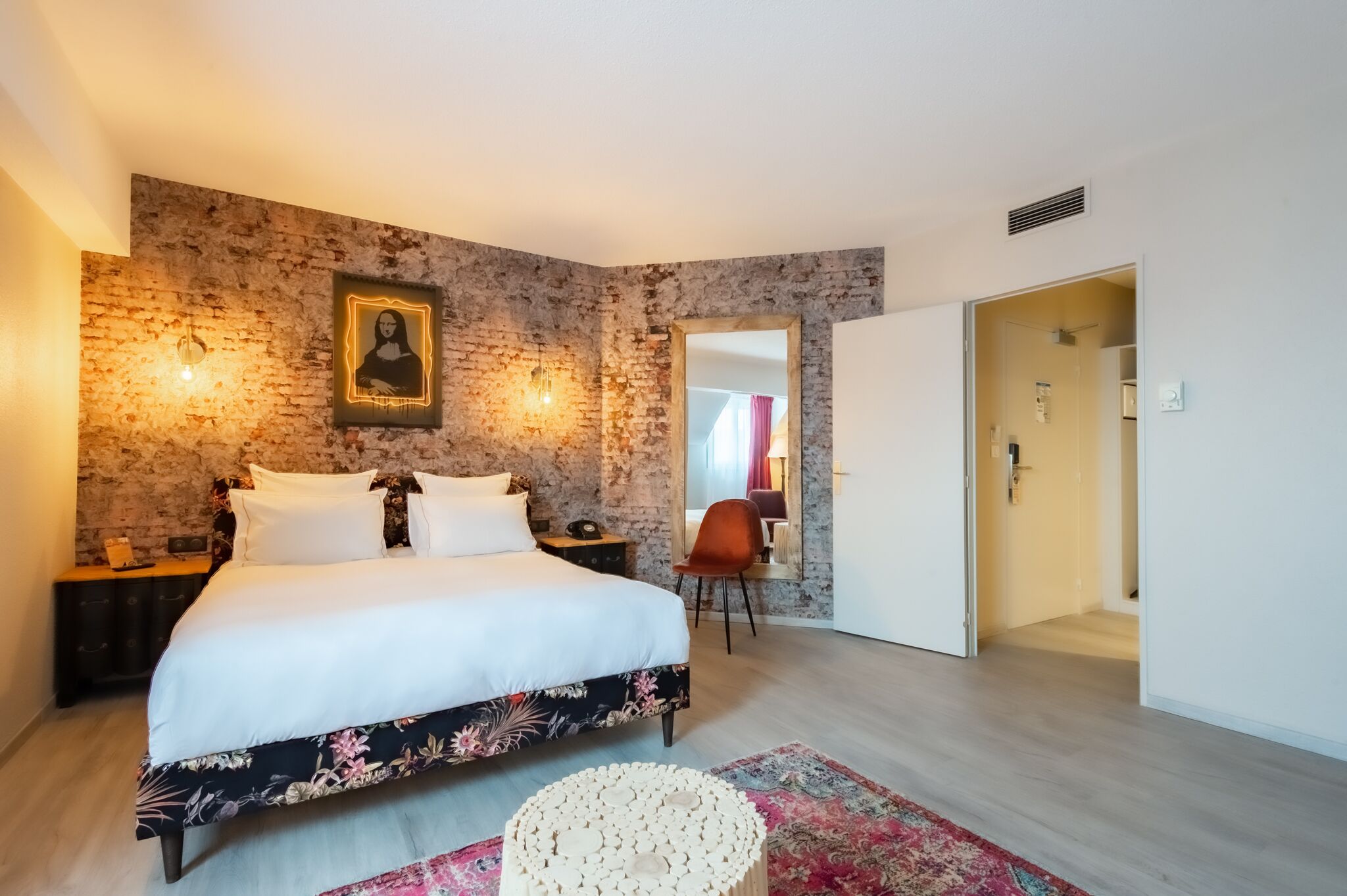 A bedroom with a large bed, a brick wall, a portrait, and a door leading to another room.