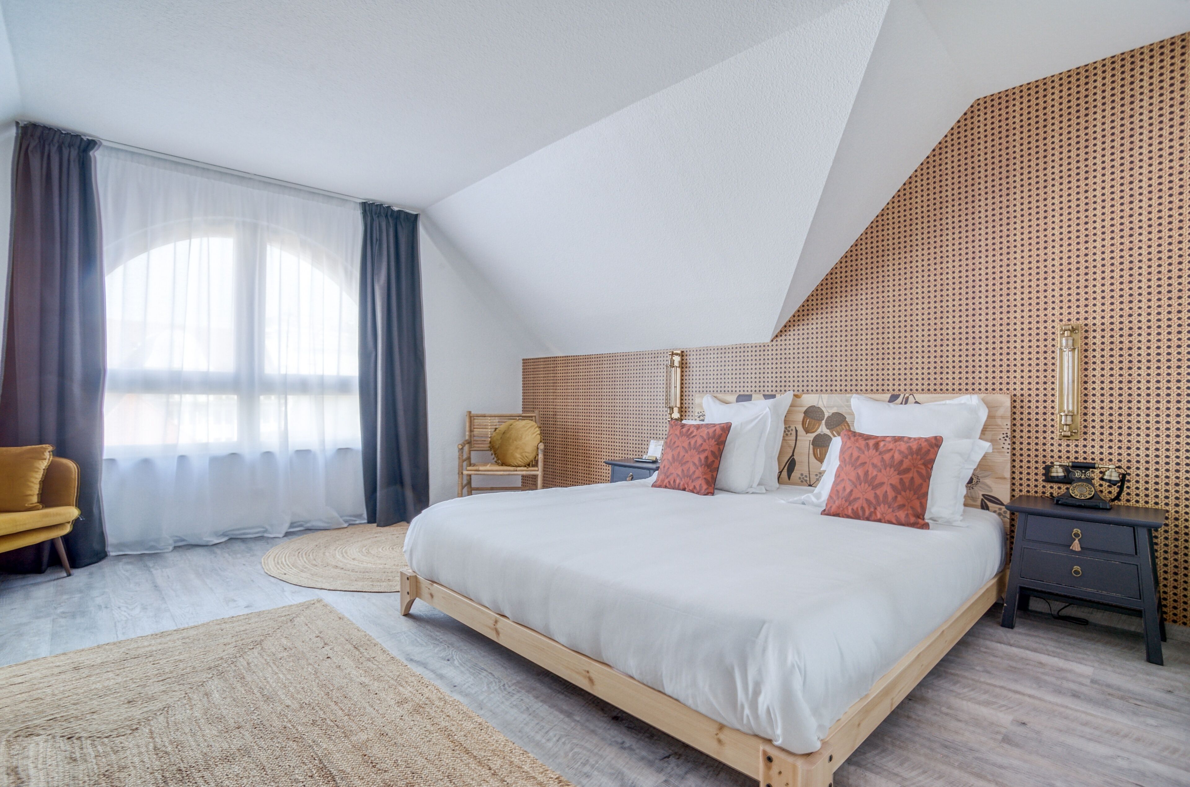 Une chambre à coucher moderne avec un grand lit, une table de chevet en bois, une chaise et un mur décoré d’un motif.