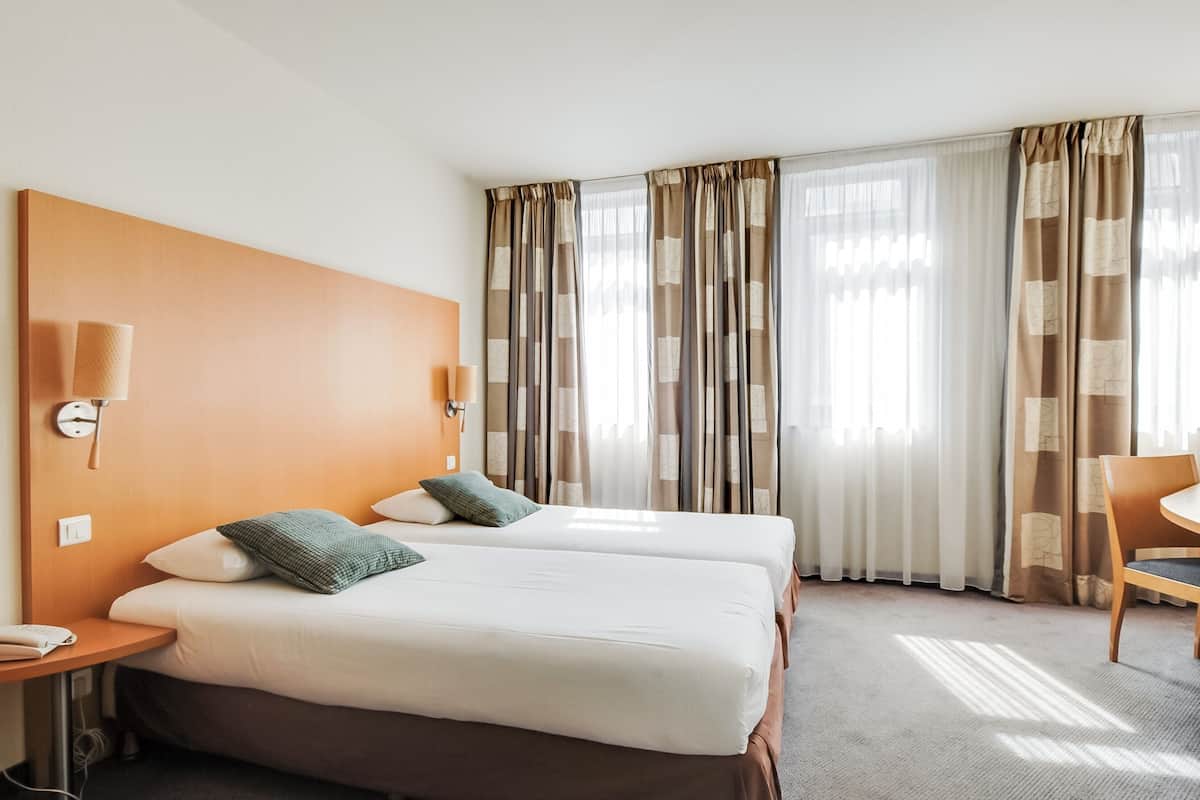 Ein Hotelzimmer mit zwei Betten, einem Holzkopfende, einem Schreibtisch mit Lampe und einem Sessel.