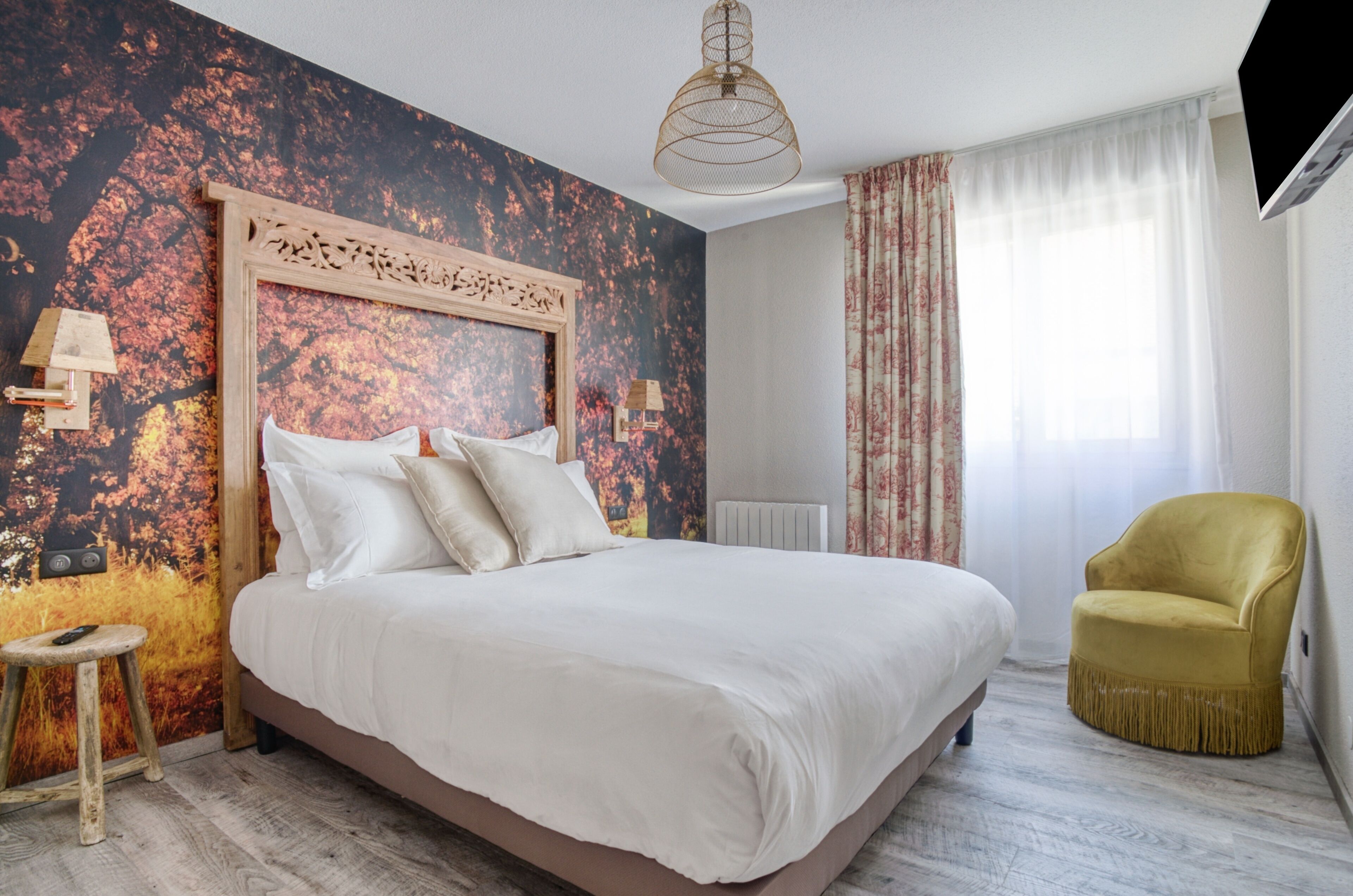 Una camera da letto con un letto grande, una testiera in legno, uno sgabello, una poltrona gialla e una finestra con tende.