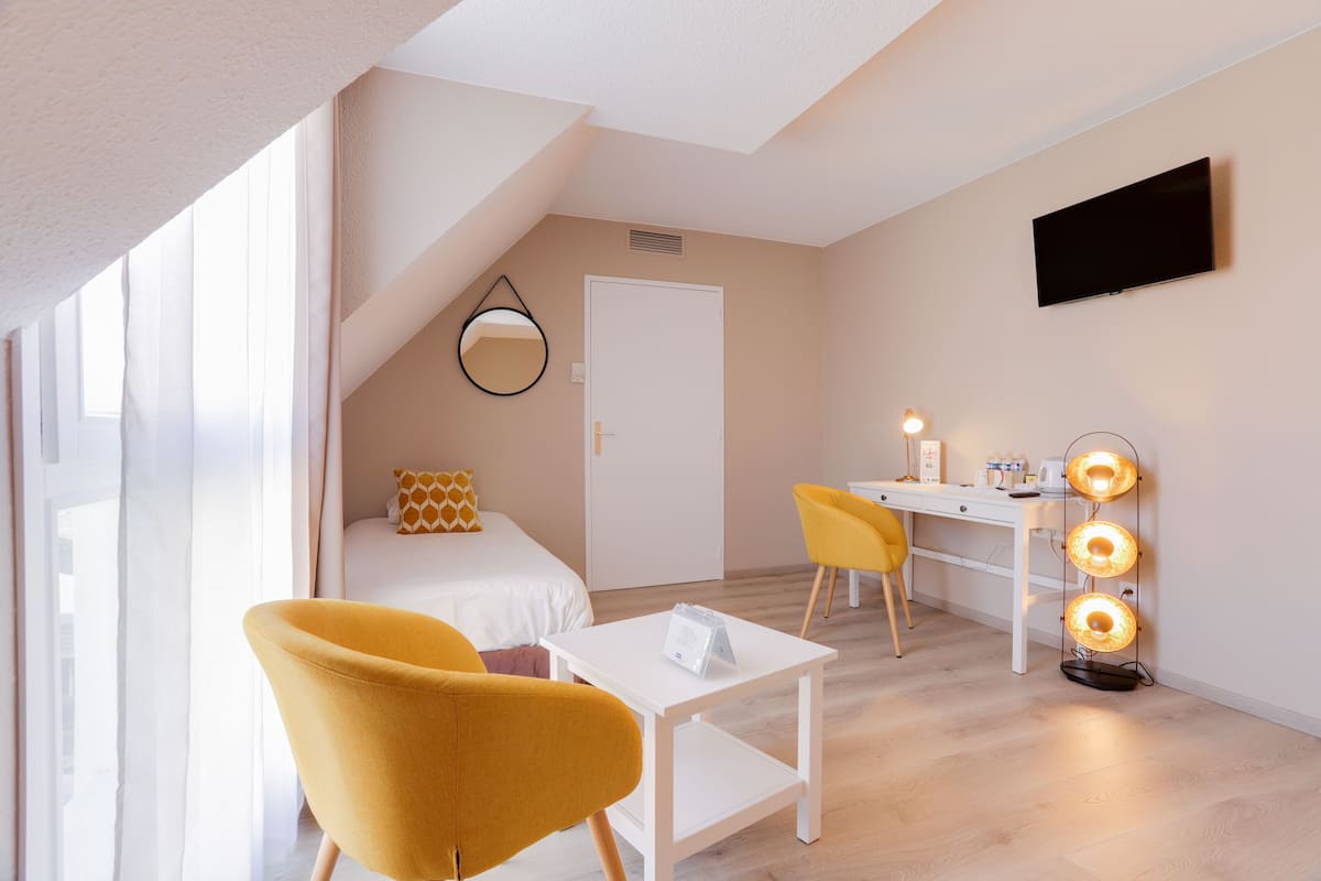 Ein modernes Hotelzimmer mit Bett, Schreibtisch, Stuhl, kleinem Tisch und einem an der Wand befestigten Fernseher.