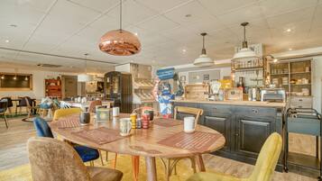 A spacious dining area with a wooden table and chairs, a kitchen in the background, and a ceiling with recessed lighting.