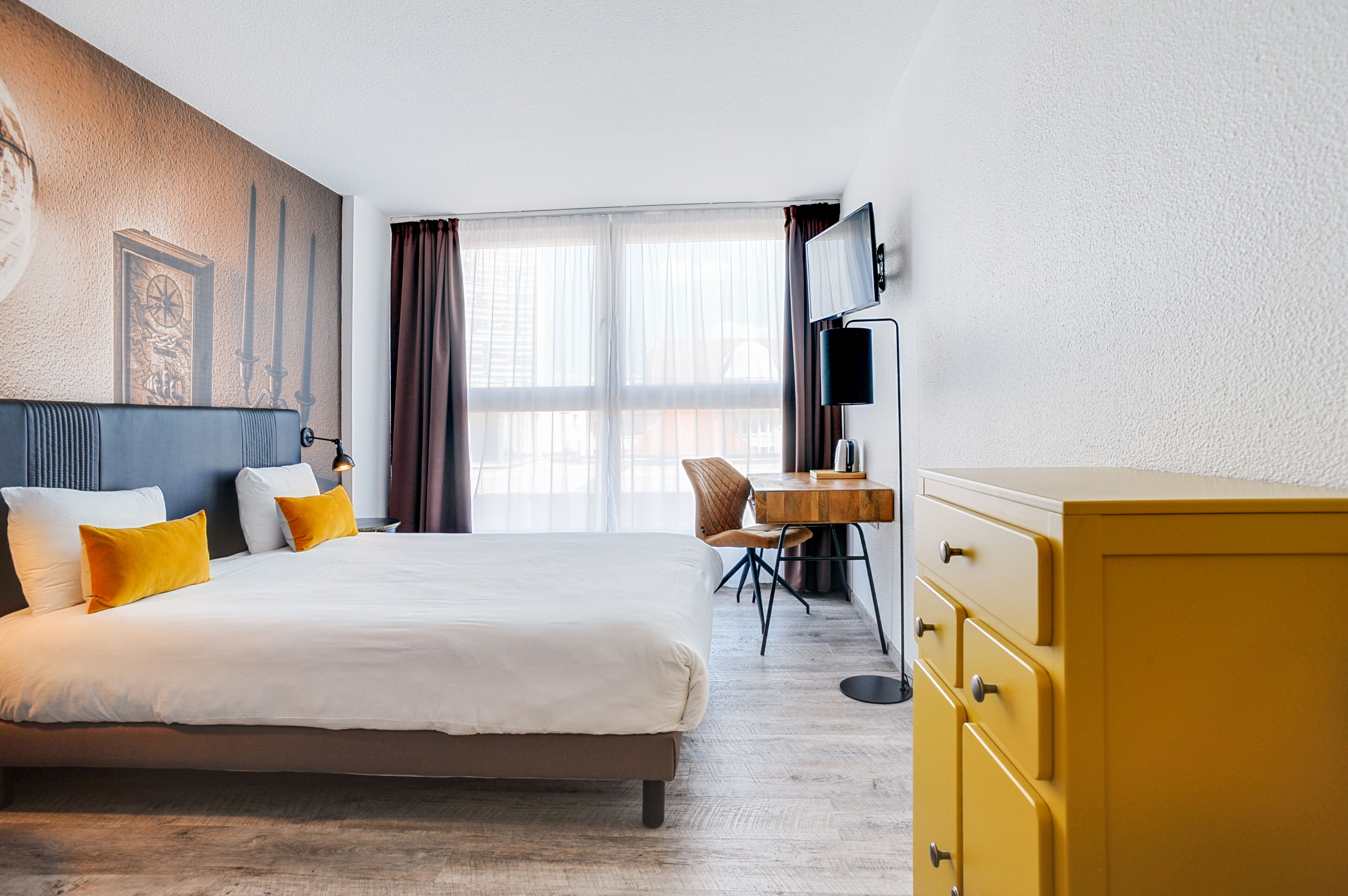 A hotel room with a large bed, a wooden desk, a television, and a yellow dresser.