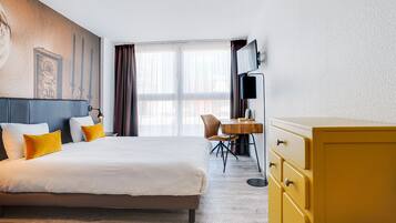 A hotel room with a large bed, a wooden desk, a television, and a yellow dresser.