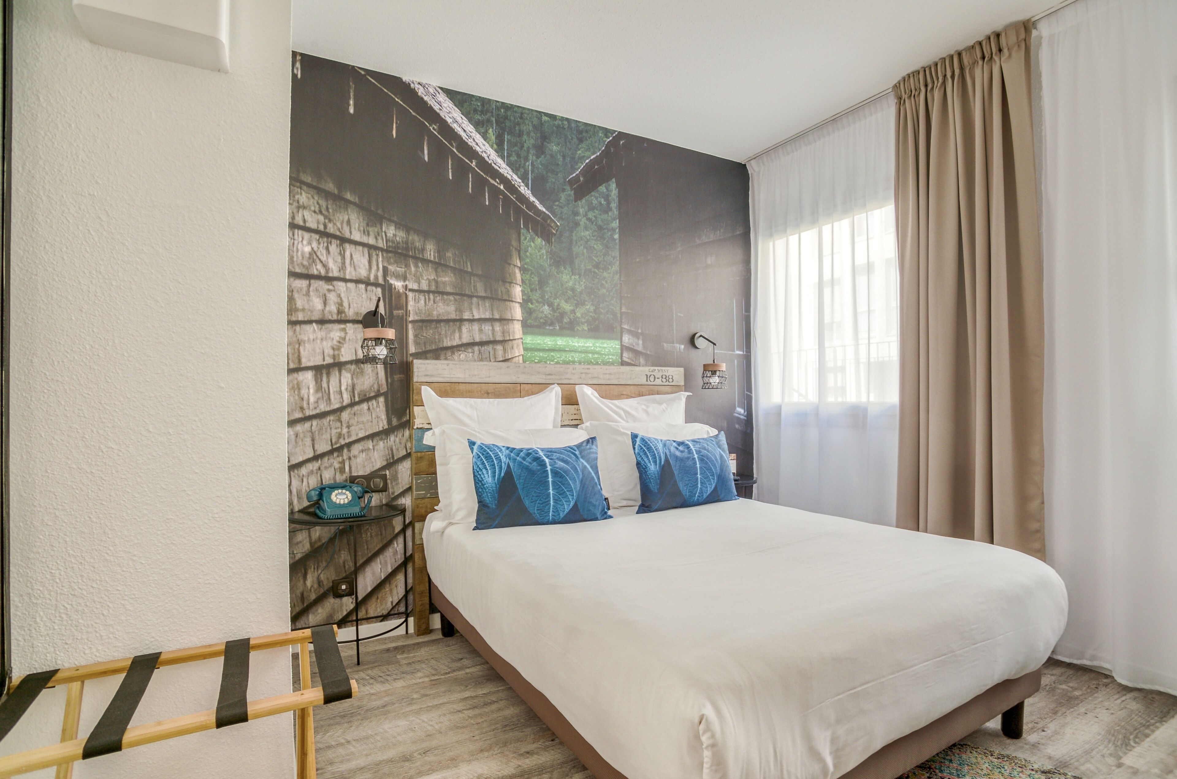 A hotel room with a large bed, a nightstand, a lamp, and a window with curtains.