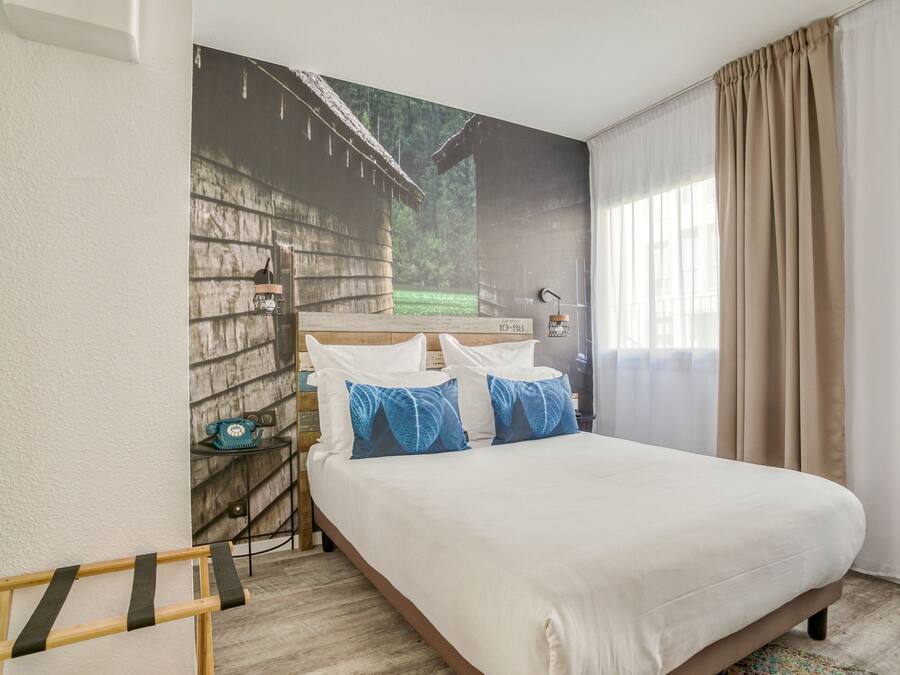 A hotel room with a large bed, a nightstand, a lamp, and a window with curtains.