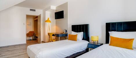 A hotel room with two beds, a desk, a chair, a TV, and a lamp.
