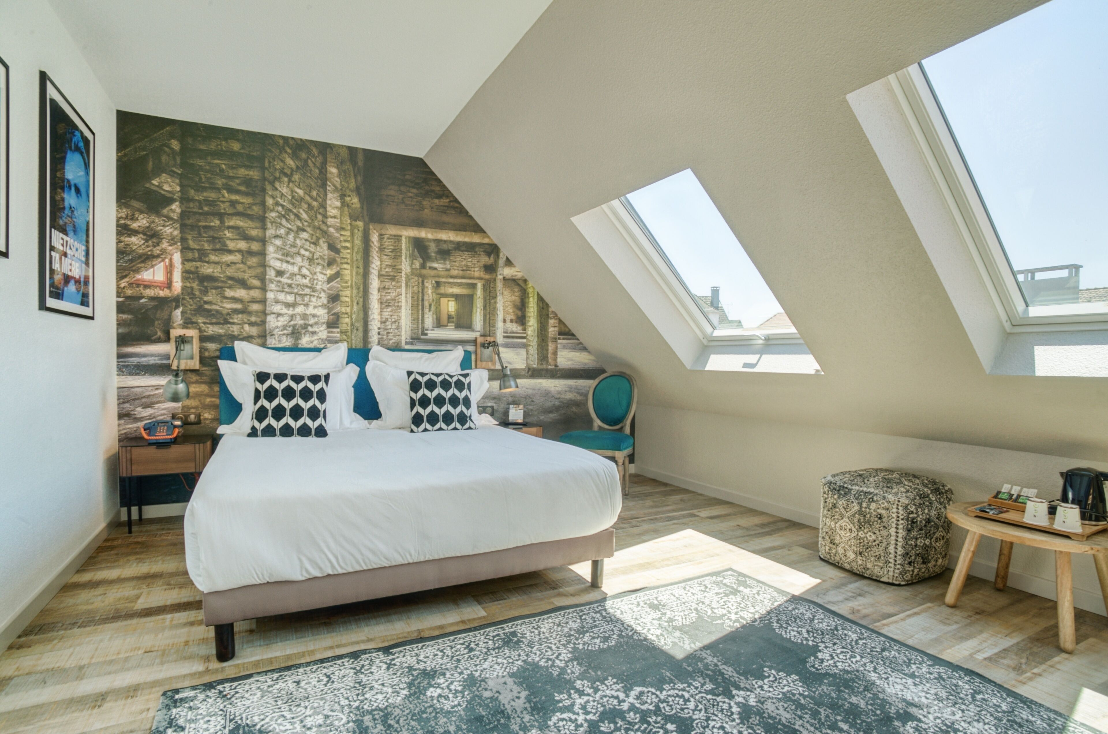 Une chambre avec un grand lit, une lucarne, une fresque murale et une petite table sur laquelle sont posés quelques objets.