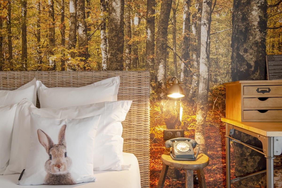 Ein Schlafzimmer mit einem Bett, weißen Kissen, einem Rattan-Kopfstück, einem alten Telefon und einem Nachttisch mit Schubladen.