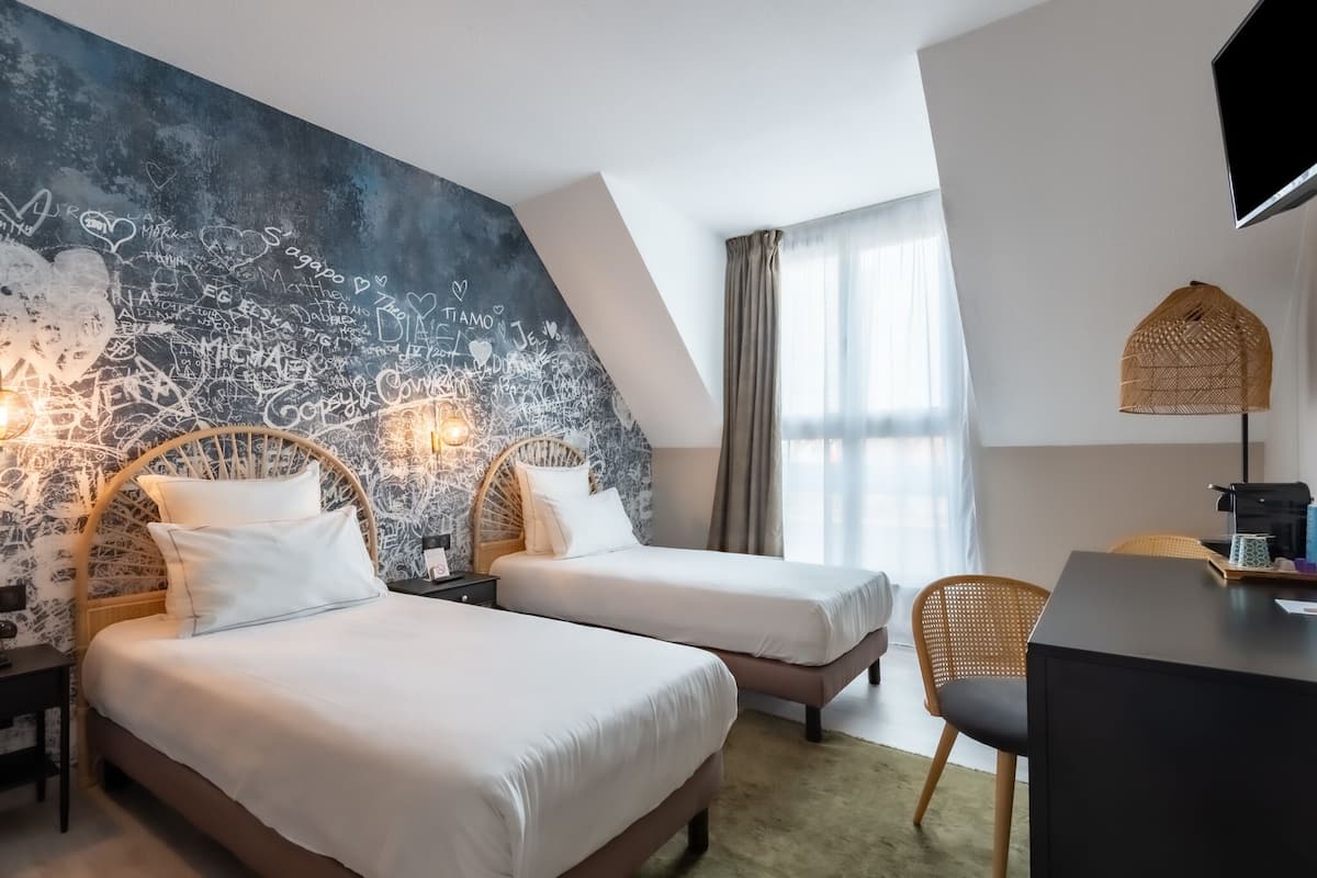 Ein Hotelzimmer mit zwei Betten, einer großen Wandtafel mit Schrift, einem Schreibtisch mit Stuhl und einem an der Wand montierten Fernseher.