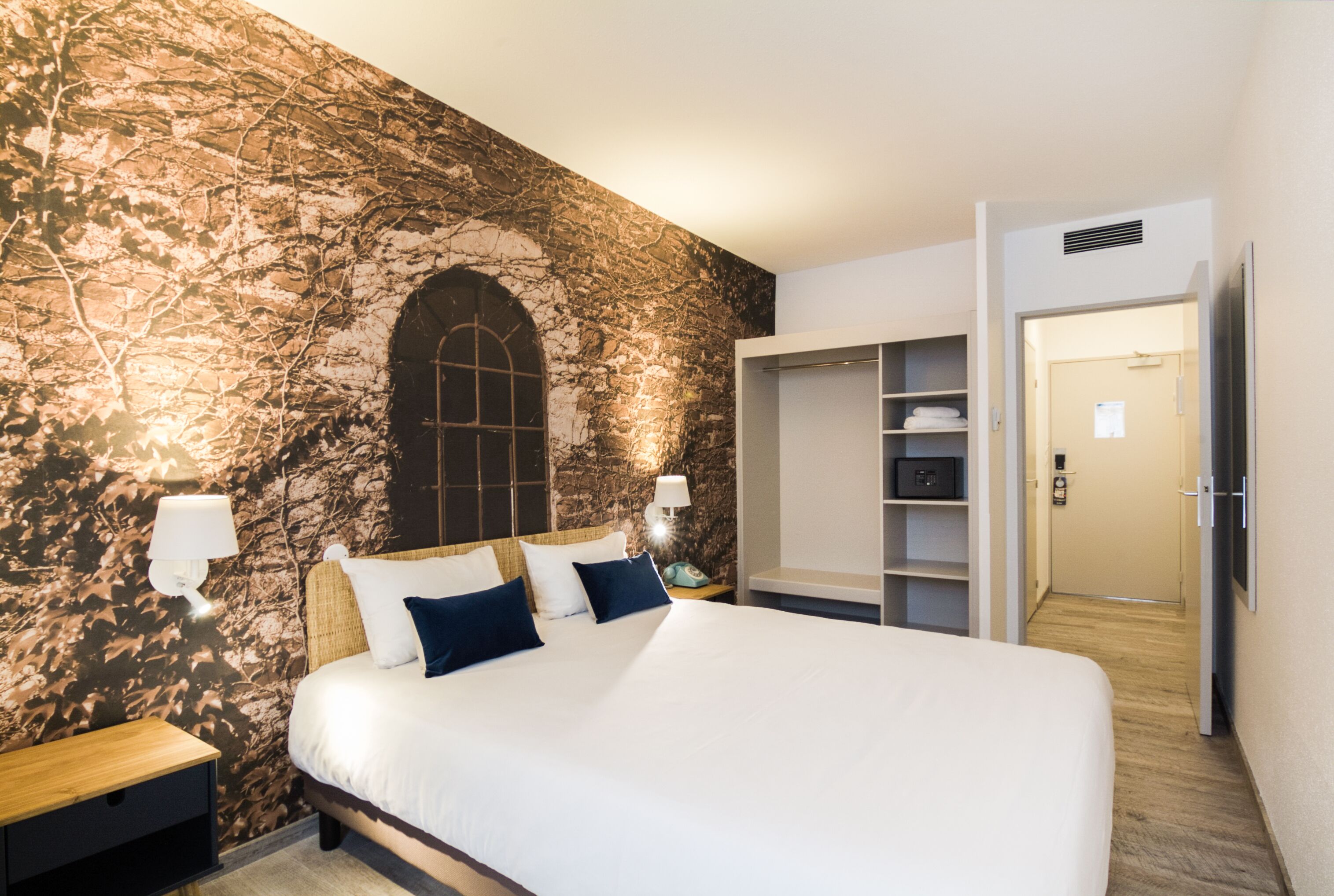 Ein Hotelzimmer mit einem großen Bett, einem Kleiderschrank, einem Nachttisch und einer Wand mit strukturierter Oberfläche.