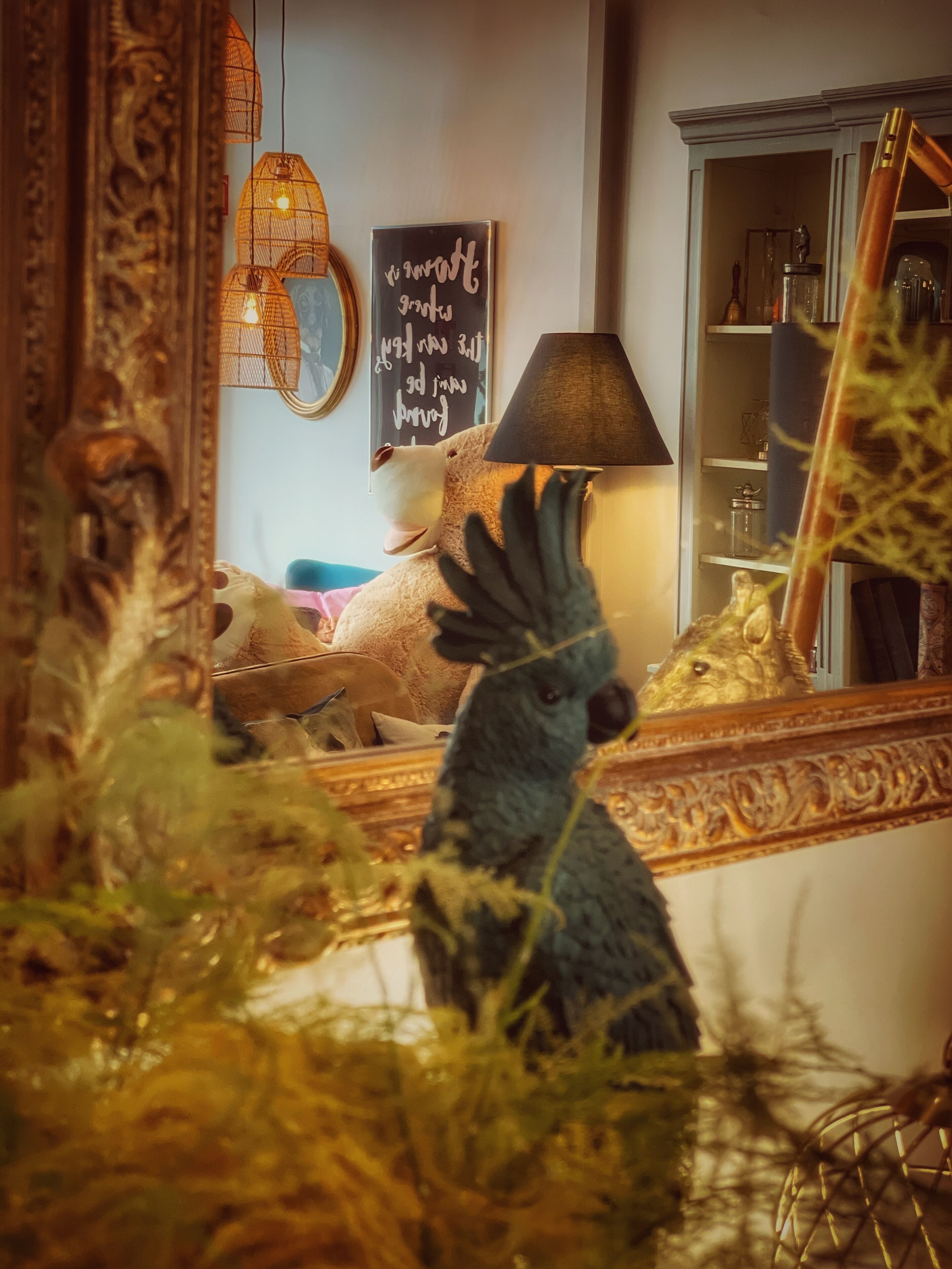 Una habitación con un espejo grande que refleja un osito de peluche, una lámpara y una pared con una frase motivadora.