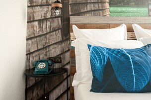 Una cama con almohadas blancas y azules, un cabecero de madera, un teléfono antiguo verde con dial giratorio sobre una mesita y una lámpara colgante.