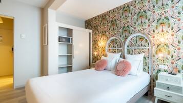Een slaapkamer met een groot bed, witte muren, bloemenbehang en een witte nachtkastje met een lamp.