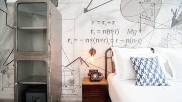 Una habitación con una caja fuerte grande, una cama, una mesita de noche con lámpara, y una pared con ecuaciones y diagramas matemáticos.