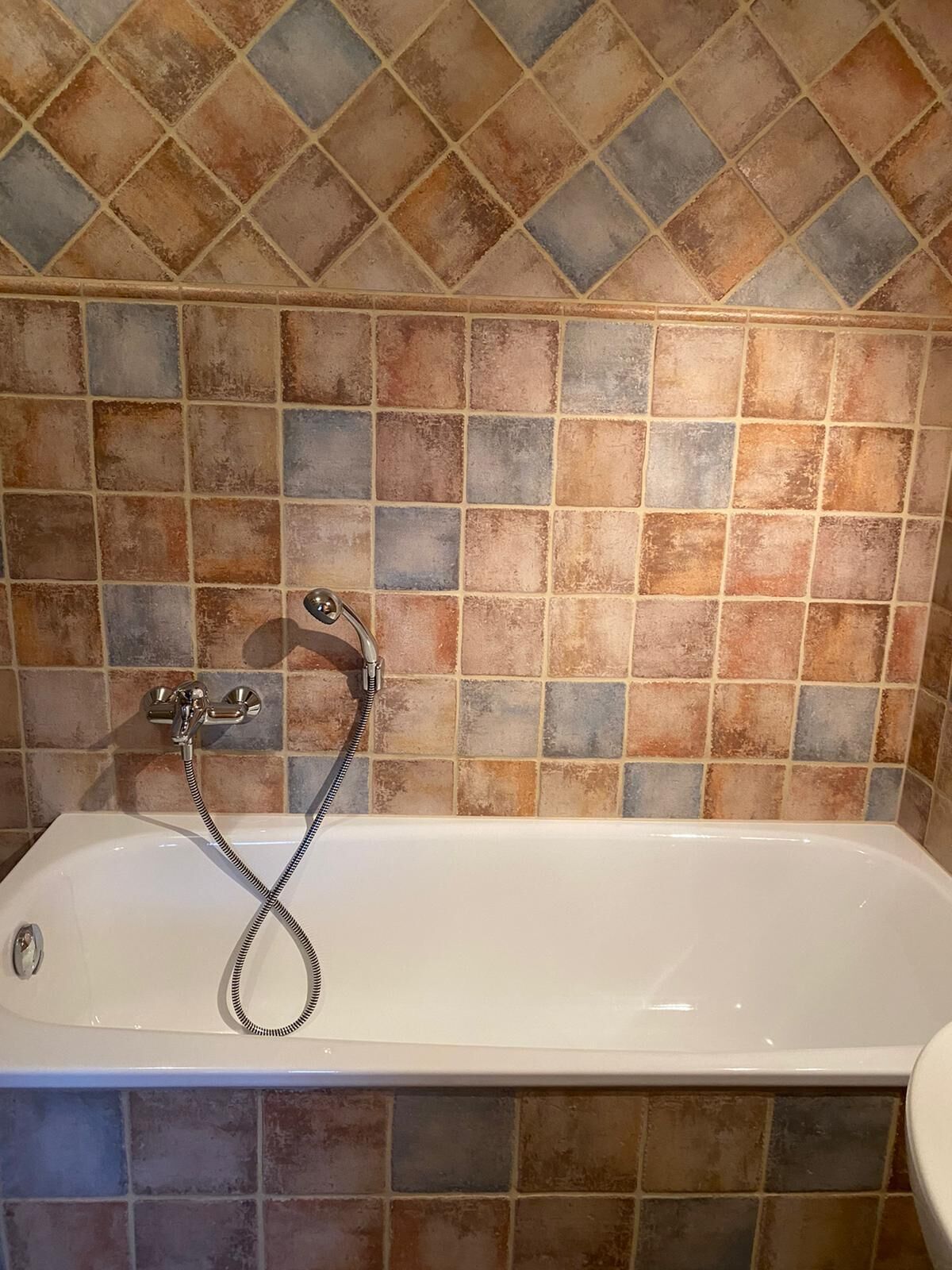 A bathroom with a white bathtub, a handheld showerhead, and a tiled wall with a diamond pattern.